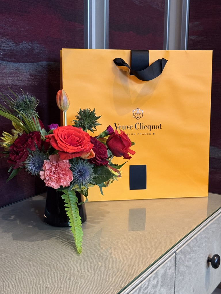 Petite floral arrangement paired with a Veuve Clicquot gift bag